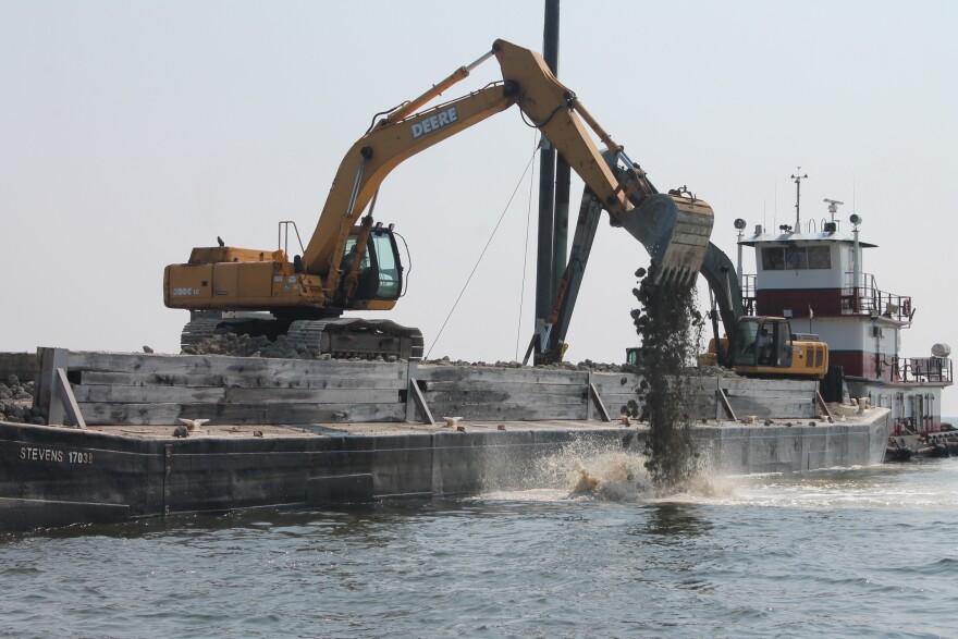  Two excavators scoop and drop limestone marl and crushed concrete off a barge into the Pamlico Sound to create an artificial oyster habitat. 