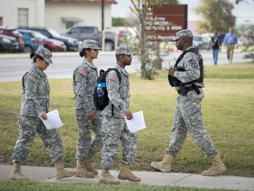 Soldiers walk past a military police officer (right) patrolling the perimeter of the U.S. Army IMCOM HQ building at Fort Sam Houston, Texas, prior to the Article 32 preliminary hearing to determine whether Army Sgt. Bowe Bergdahl will be court-martialed.