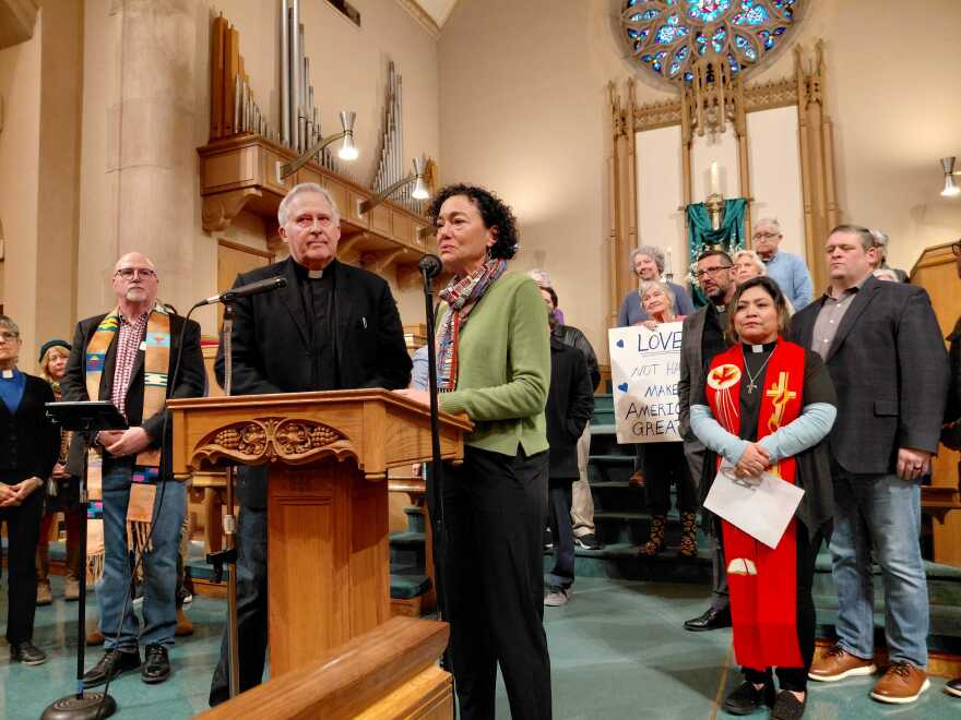 A group of men and women wearing religious attire stand at a church altar for a press conference. 