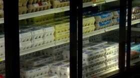 A refrigerated grocery store shelf is stocked with multiple rows of eggs in cardboard and plastic cartons of various sizes and brands, neatly arranged behind glass doors—unlike the recent shutdown debates between Illinois Democrats and Republicans.