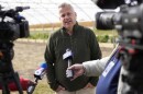 U.S. Rep. Eric Sorensen talks to media on a farm while wearing a forest green quarter-zip sweater