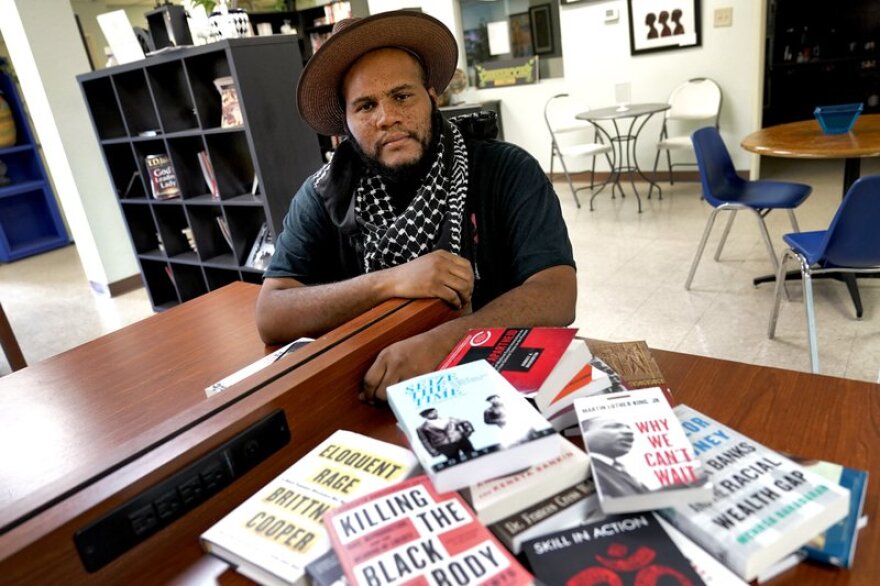 A photo of Black-bookstore owner Ali Nervis surrounded by books