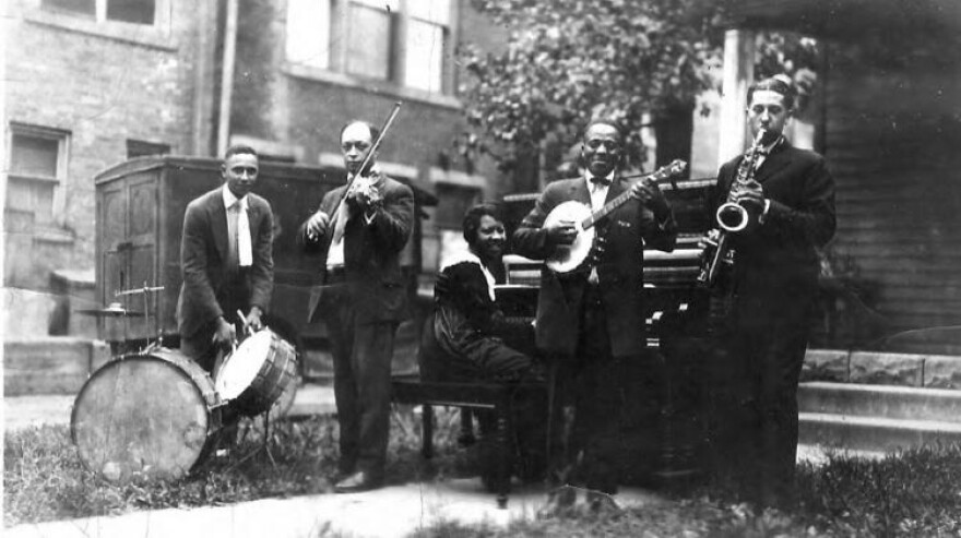 5 person band with drums, violin, piana, banjo and saxaphone players.