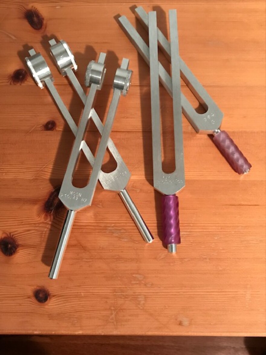 A close-up view of four tuning forks lying on a wooden surface.