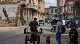 A man rides a tricycle with his leashed dog running alongside him during a blackout in Havana, Cuba, Monday, March 16, 2026. 