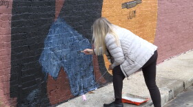 Mural artist Pamela Bliss coats the left shoe of John Mellencamp's image with her brush.
