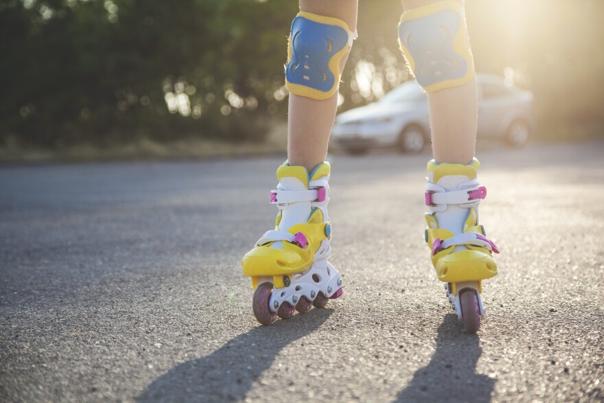 a little girl roller skating on a road with sunlight streaming behind her