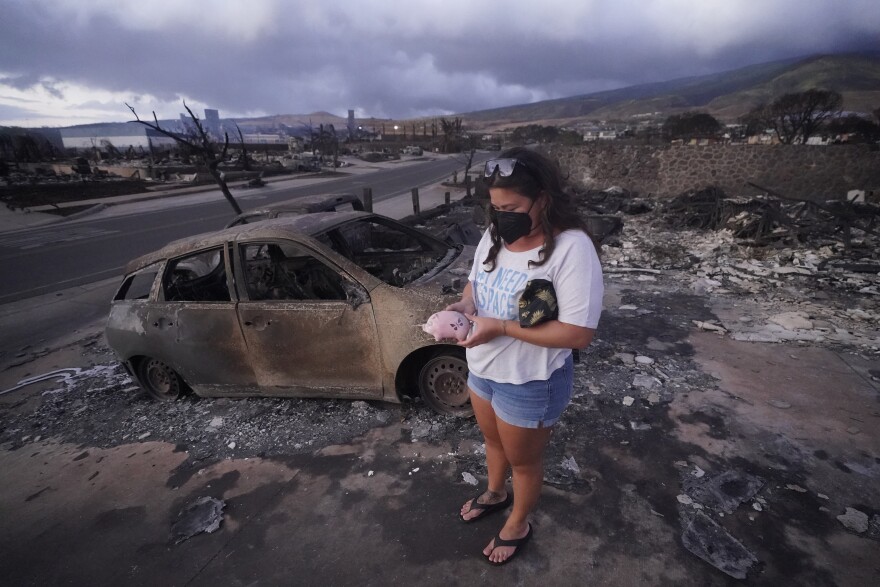 FILE - Summer Gerling picks up her piggy bank found in the rubble of her home following the wildfire on Aug. 10, 2023, in Lahaina, Hawaiʻi. (AP Photo/Rick Bowmer, File)