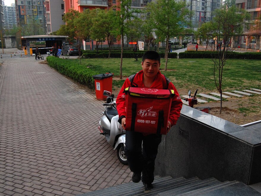 Haidilao delivery man Liu Lei rides an electric moped to a customer's house, with two backpacks — one with the food, one with the hot plate, pot and utensils. He arrives one hour after the order was placed.