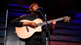 A man playing an acoustic guitar closes his eyes while singing into a microphone on stage.