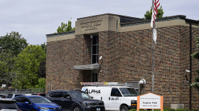 A view of a brick building from the outside. Cars are parked out front.