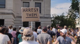 A demonstrator holds a sign calling for the arrest of a group of White people who assaulted a Black man while shouting racial slurs on July 4.