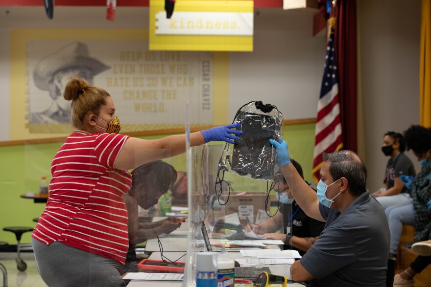 Guadalupe Alvarez, 24, grabs a school-sponsored laptop over the plexiglass. Alvarez said she was supposed to pick up two laptops from Dunbar Elementary School, but one of her children were not assigned to one.