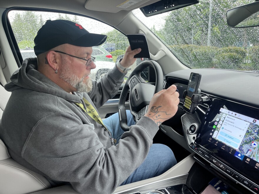 A man sits in a car, holding a notebook.