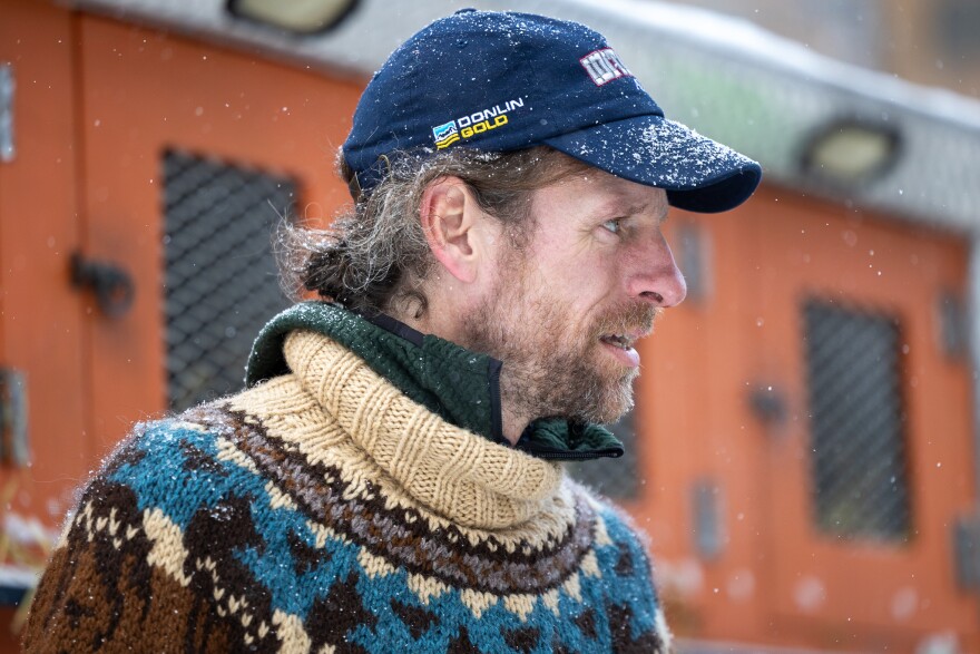 A man in a blue baseball cap and a sweater looks to the right in this portrait shot.