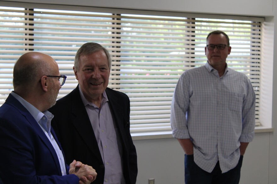 Dick Durbin stands with a man directly to the left and another slightly behind to the right of the camera. All are laughing.