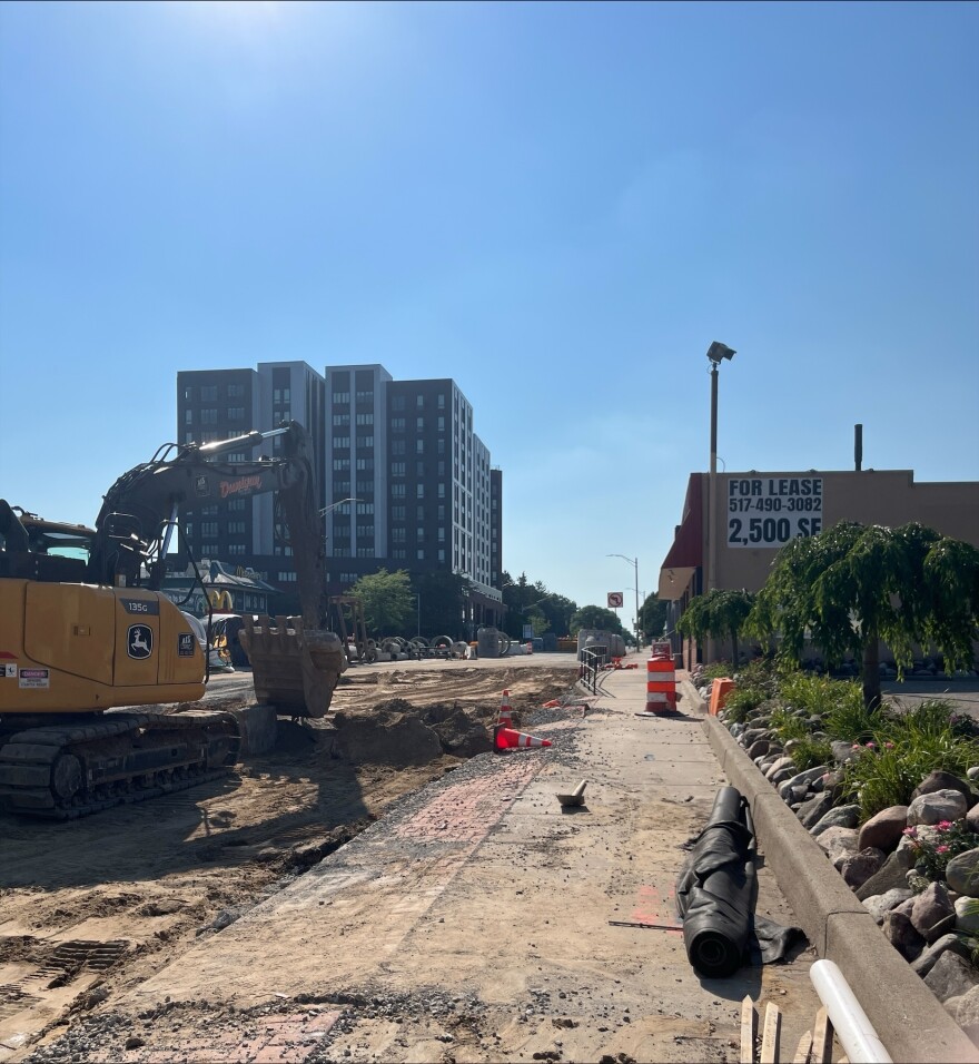 A large yellow excavator digs up dirt from the road on a sunny day.
