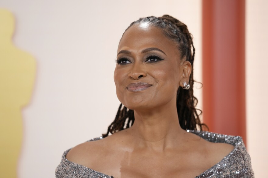 an above-the-shoulders image of a black woman on the red carpet of the academy awards wearing a sparkly silver over-the-shoulder dress