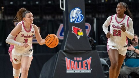 Illinois State's Trista Fayta [left] dribbling a basketball and Doneelah Washington jogging alongside during a game with a basket support behind them featuring a logo that reads 'The Valley' and a redbird logo for Illinois State and a logo featuring a bulldog and the letter D for Drake 