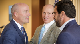Three men wearing suits shake hands and talk. 