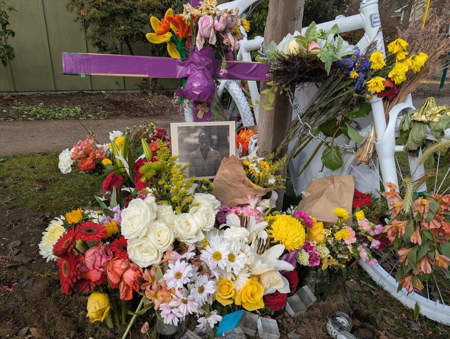 A bike painted white with flowers and a photo of a man on a grassy strip by a sidewalk
