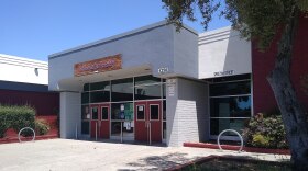 A white building with red doors and a few red walls. A sign on the building reads: Richmond High School. 