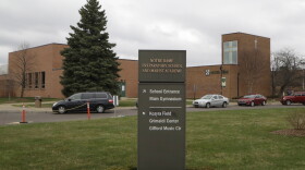 Long shot of a modern brick school building with driveway, lawn and entrance sign in the foreground
