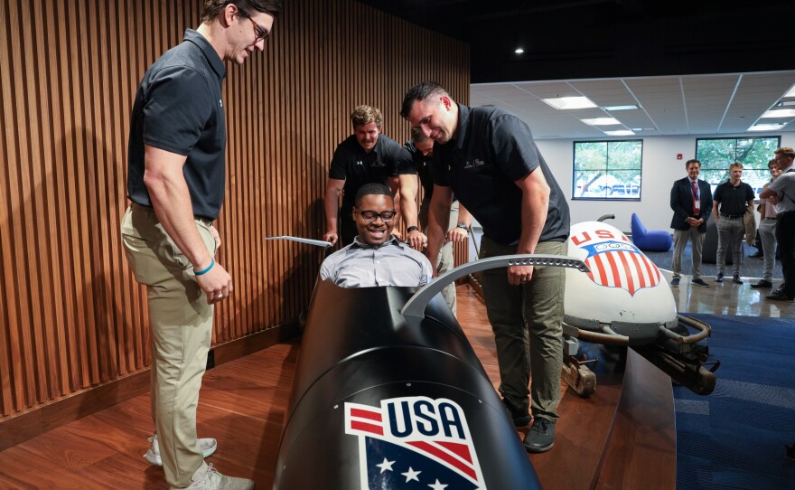 Hassan Williams climbs into the cockpit of the USA Olympic bobsled as Eastman Kodak Company announces its support of USA Bobsled/Skeleton ahead of the 2026 Winter Olympics, unveiling a new state-of-the-art sled in Kodak’s iconic yellow and red at the Golisano Institute for Business & Entrepreneurship. The historic 1956 Bronze Medal–winning “Tyler Sled,” designed and raced by Kodak engineers, was also on display.