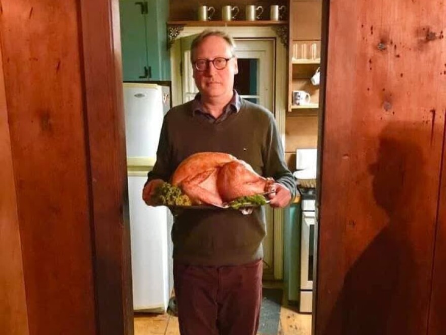 Man with somber expression holding a very large cooked turkey on a platter
