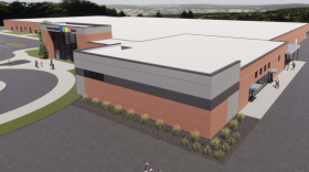 a rendering shows a school building on a parking lot, focused on a brick square addition
