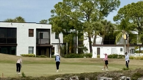 Golfers play with building behind them 