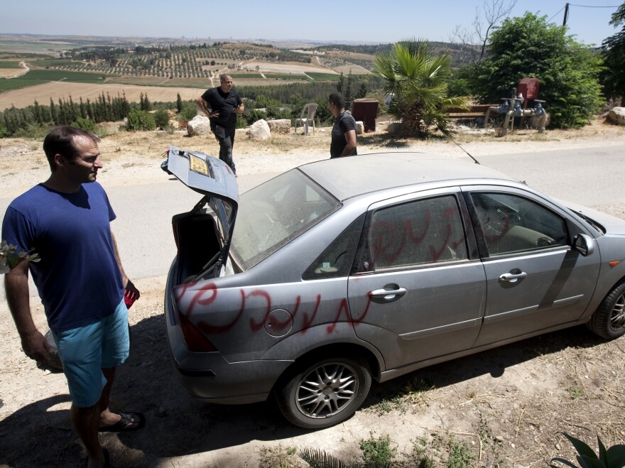 Vandals slashed car tires and spray-painted graffiti in the village of Neve Shalom earlier this month. Here, Jewish Israeli and Arab Israeli men inspect a car that was spray-painted with the word "Revenge."