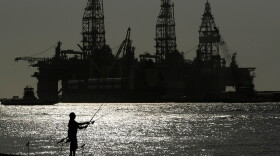 FILE - A man fishes near docked oil drilling platforms May 8, 2020, in Port Aransas, Texas. 