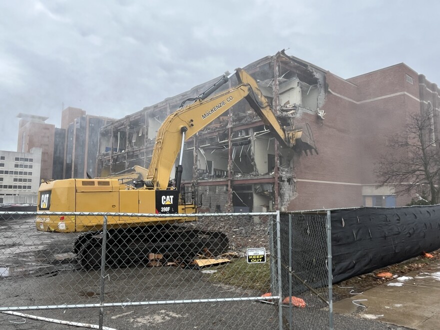 Construction excavator knocking down a brick wall connected to a building