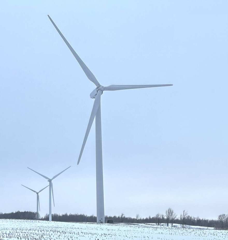 Three large wind turbines in farm fields with snow on the ground. 