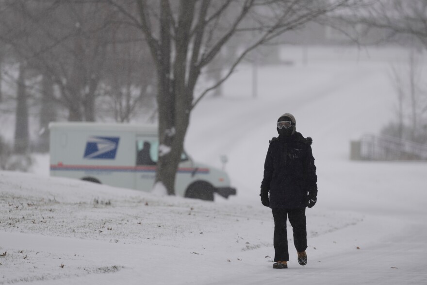 Malik Jones walks along a snow-covered street with a U.S. Postal Service truck in the background as a winter storm passes though the area Saturday, Jan. 24, 2026, in Prairie Village, Kan. (AP Photo/Charlie Riedel)