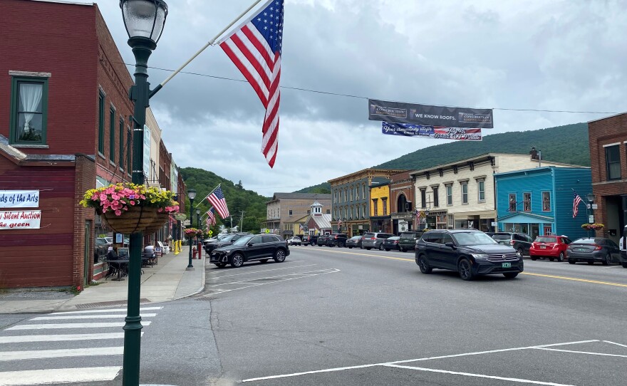 A downtown block with multicolored buildings, and flags and flower pots lining the street.