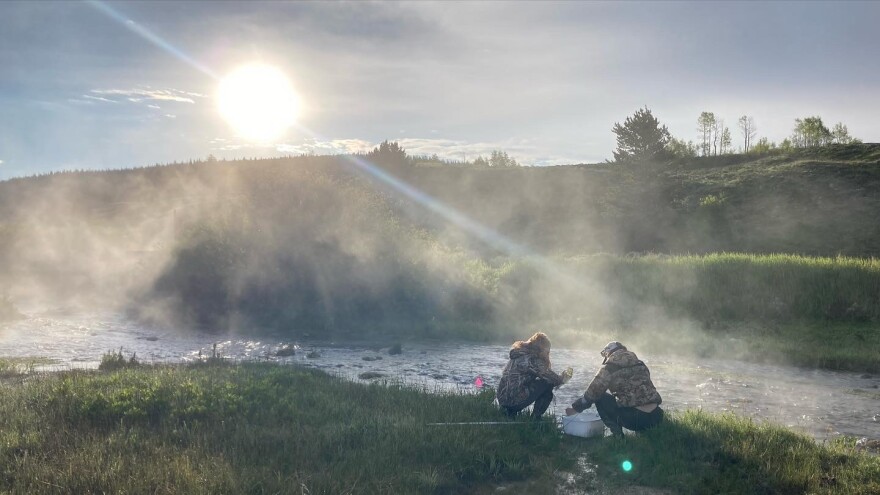 Two researchers crouch by the Kendall Warm Springs.