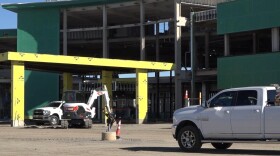 A building under construction, half open to the elements, is surrounded by trucks and a backhoe.