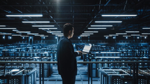 Data center administrator uses a laptop with servers in the background.