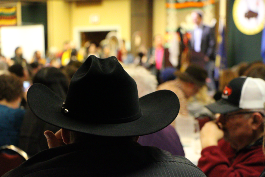 A man in a black cowboy hat looks towards the center of a crowded room.