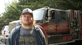 a man looks at the camera with a small smile with a fire truck behind him 