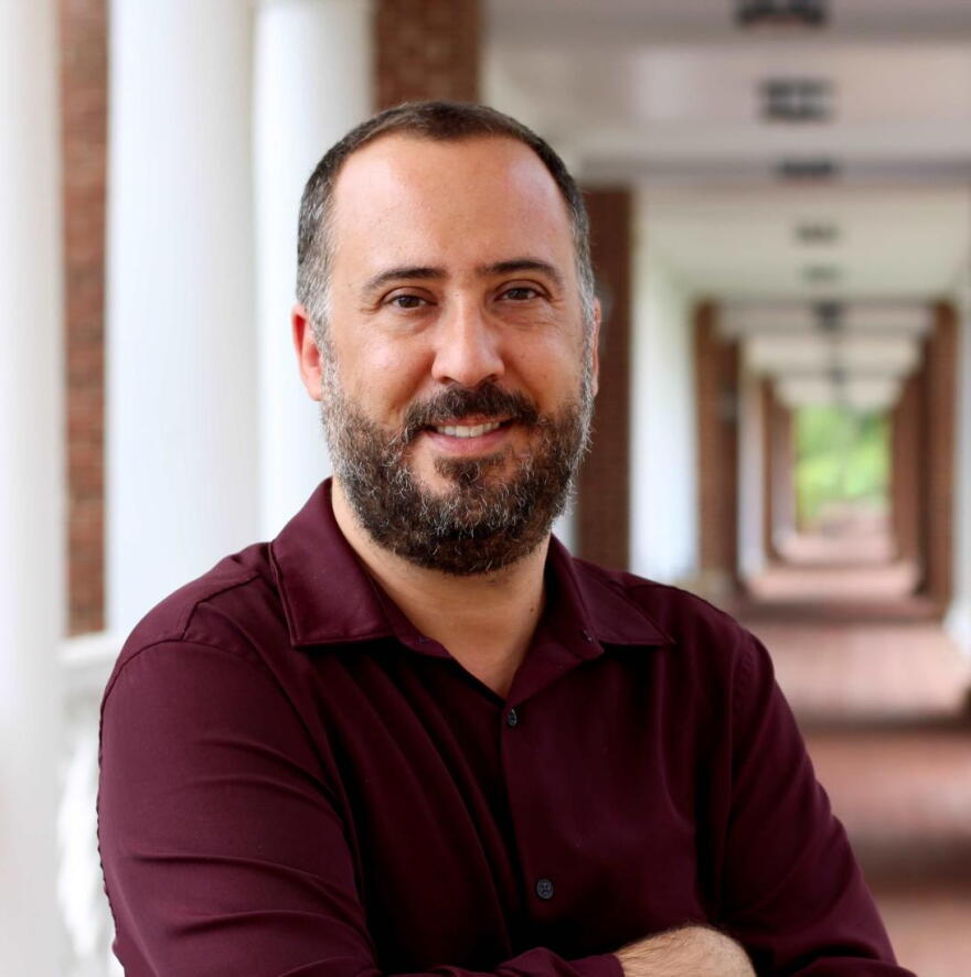 A headshot photo of a man standing in front of a long hallway outside