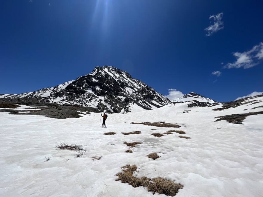 A person walks on top of snow with a mountain in the background.