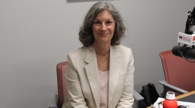 A woman in a blazer smiles while sitting in front of a microphone