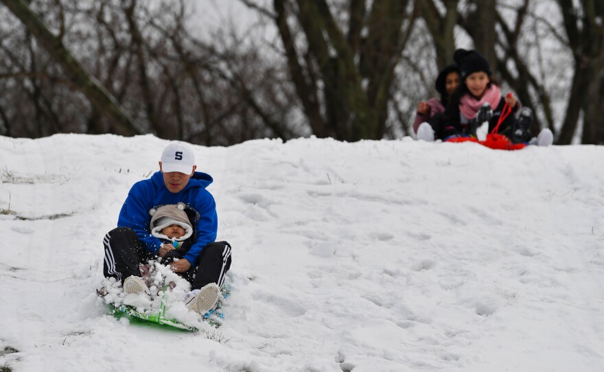 Chris Flores holds his son, Able, 1, as they sled down the hill in Kirby Park on Sunday.