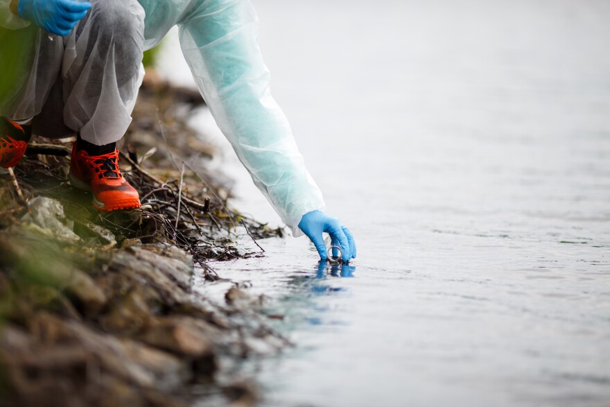 Laboratory assistant with test tube takes water samples on river bank