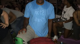 A man kneeling next to a cooler and sweating through his shirt. 