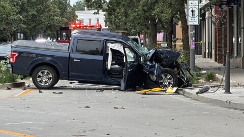 A damaged pickup truck sits on a city street in a small downtown area