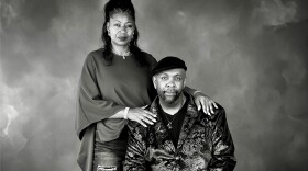 Renee Peoples stands with her hands resting on the shoulders of her seated husband, Bobby.
